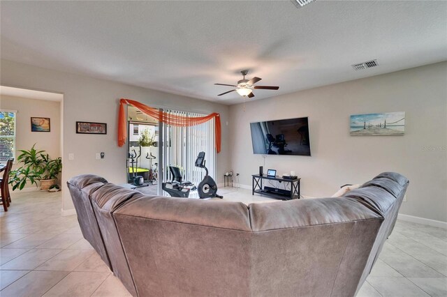 living room featuring light tile patterned floors, visible vents, baseboards, and ceiling fan