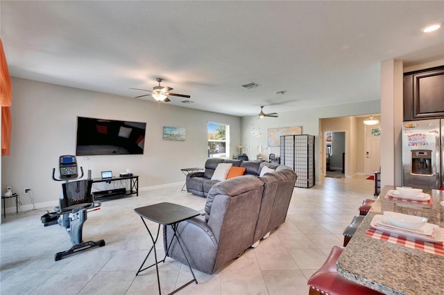 living room featuring light tile patterned floors, visible vents, baseboards, and a ceiling fan