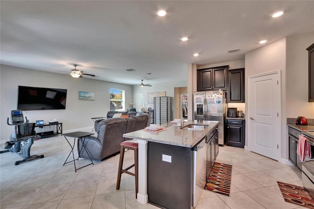 kitchen with light stone counters, a sink, stainless steel appliances, ceiling fan, and open floor plan