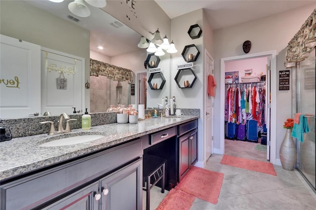 bathroom with a spacious closet, visible vents, double vanity, a stall shower, and a sink