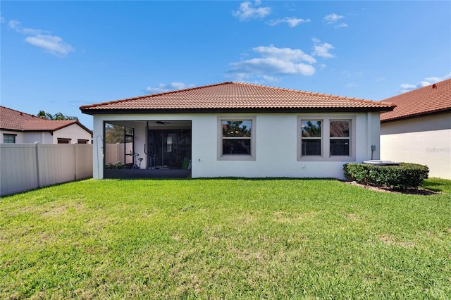 rear view of house featuring fence, a yard, a sunroom, stucco siding, and a tile roof