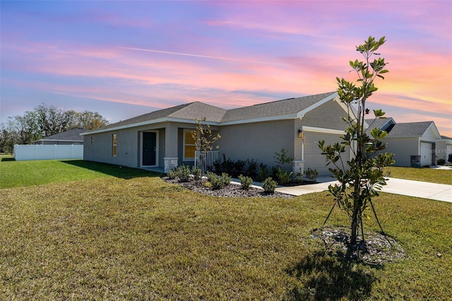 view of front of property featuring stucco siding, a lawn, fence, a garage, and driveway