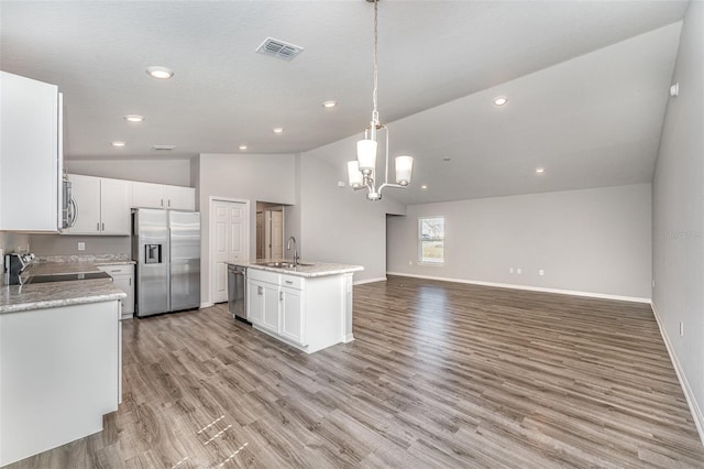 kitchen featuring stainless steel appliances, a sink, white cabinetry, open floor plan, and vaulted ceiling