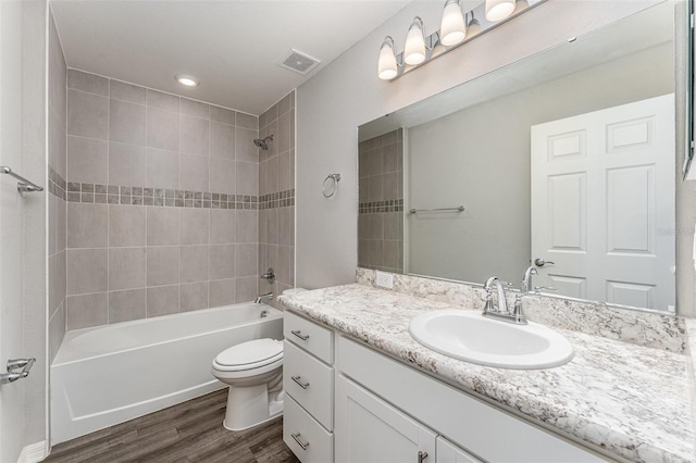 bathroom with toilet, wood finished floors, visible vents, vanity, and tub / shower combination