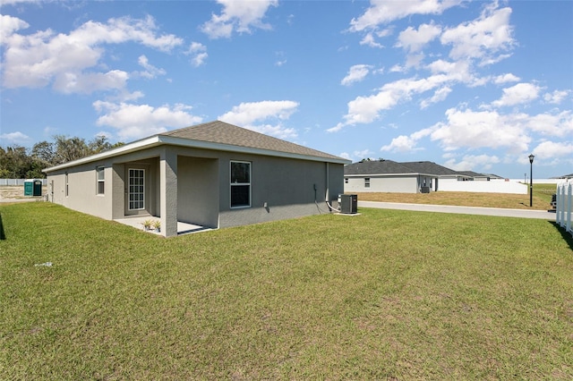 rear view of property with cooling unit, a lawn, and stucco siding