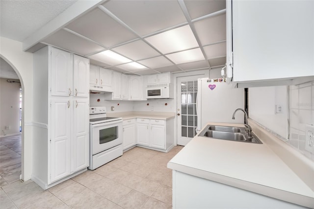 kitchen featuring arched walkways, under cabinet range hood, white appliances, a sink, and white cabinets