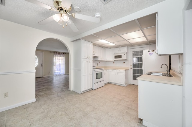 kitchen with arched walkways, light countertops, a sink, ceiling fan, and white appliances