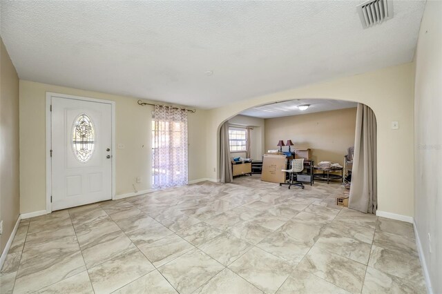 entrance foyer featuring arched walkways, visible vents, a textured ceiling, and baseboards