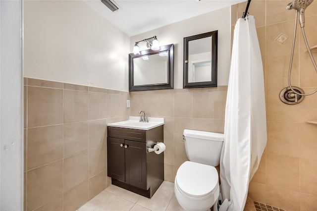 full bath with toilet, tiled shower, visible vents, and tile walls