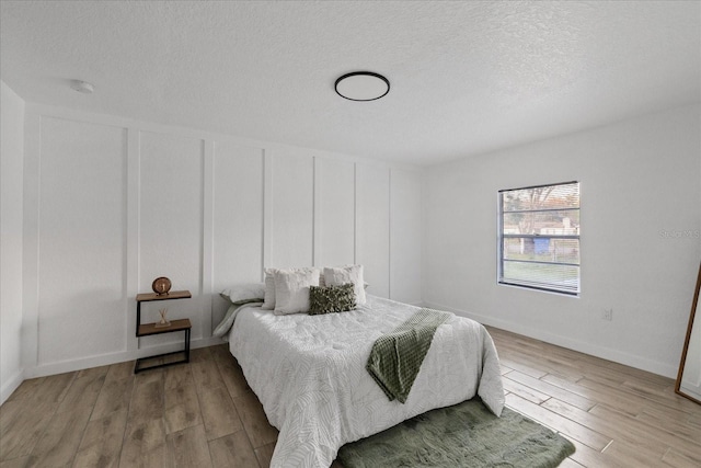 bedroom featuring a textured ceiling, baseboards, wood finished floors, and a decorative wall