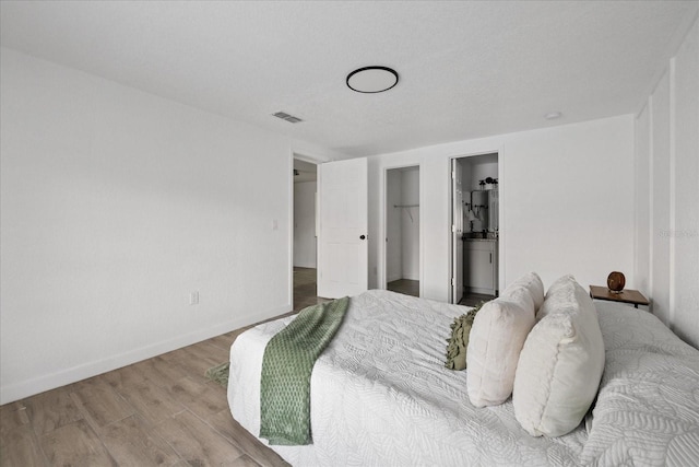 bedroom with wood finished floors, visible vents, baseboards, a closet, and ensuite bath