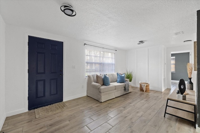 living room featuring baseboards, visible vents, light wood-style flooring, and a textured ceiling