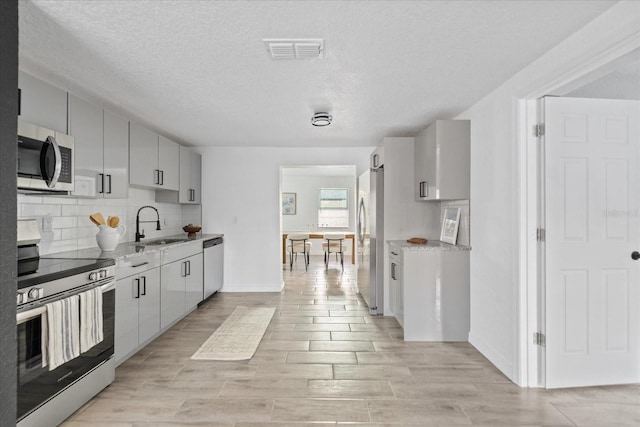 kitchen with a sink, visible vents, appliances with stainless steel finishes, backsplash, and light stone countertops