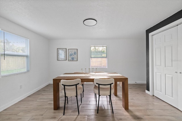 dining space with light wood-style flooring, baseboards, and a textured ceiling