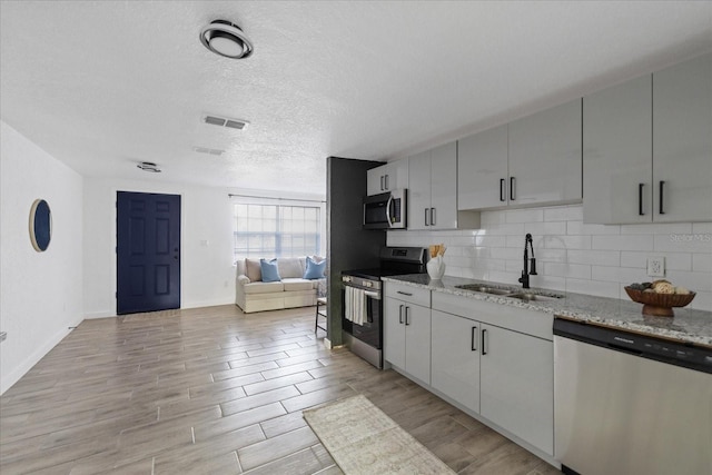 kitchen featuring wood finish floors, a sink, visible vents, appliances with stainless steel finishes, and backsplash