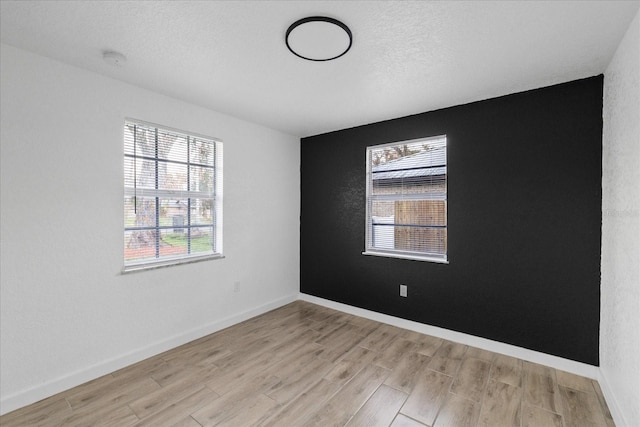 unfurnished room featuring light wood-style floors, a textured ceiling, and baseboards