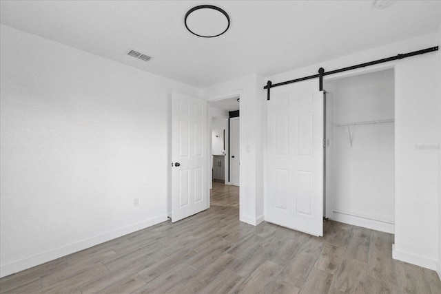 unfurnished bedroom featuring a barn door, wood finished floors, visible vents, baseboards, and a closet