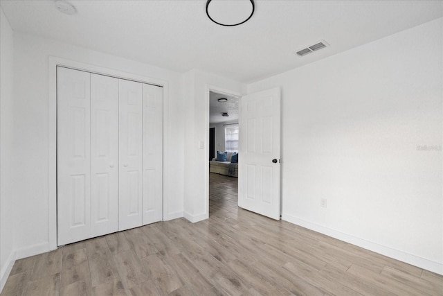 unfurnished bedroom with a closet, visible vents, baseboards, and light wood finished floors