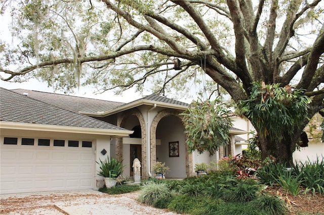 view of front facade featuring stucco siding, a garage, and roof with shingles