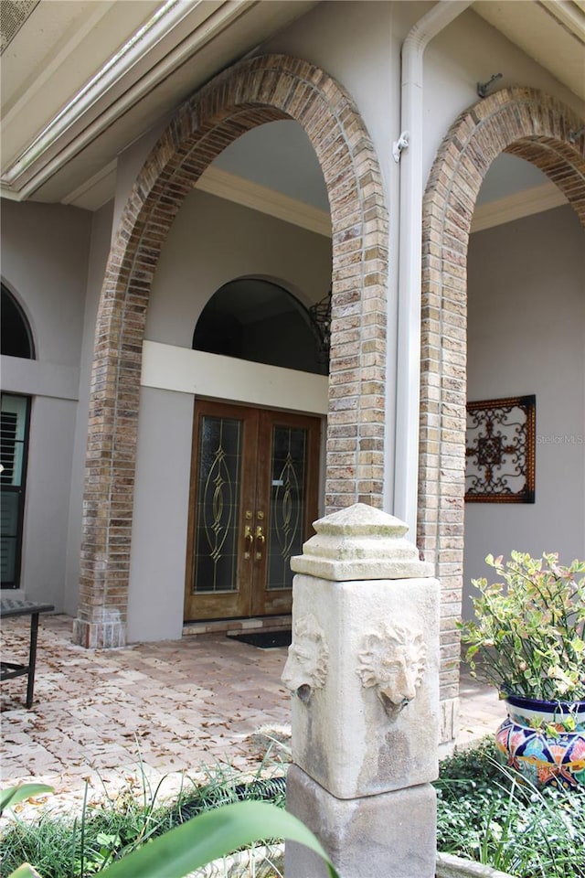 property entrance with brick siding, stucco siding, and french doors