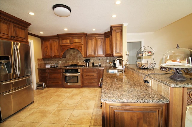 kitchen with light stone countertops, decorative backsplash, a peninsula, stainless steel appliances, and a sink