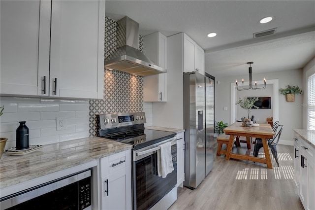 315 40th St S, Saint Petersburg, FL 33711 - kitchen featuring light wood-style floors, wall chimney exhaust hood, white cabinetry, and stainless steel appliances