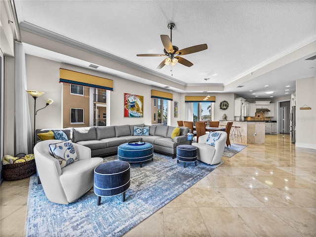 living area with a textured ceiling, ceiling fan, visible vents, ornamental molding, and a raised ceiling