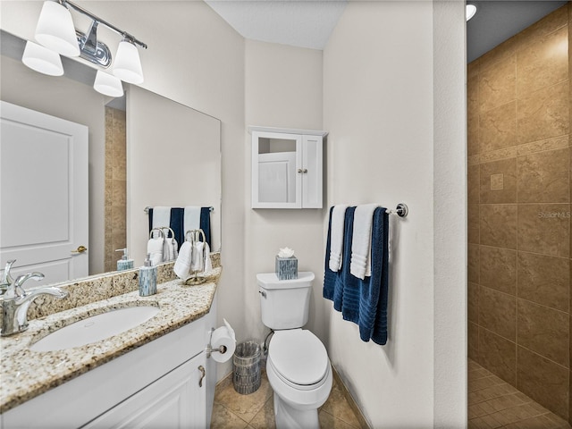 bathroom with toilet, tile patterned flooring, a tile shower, and vanity