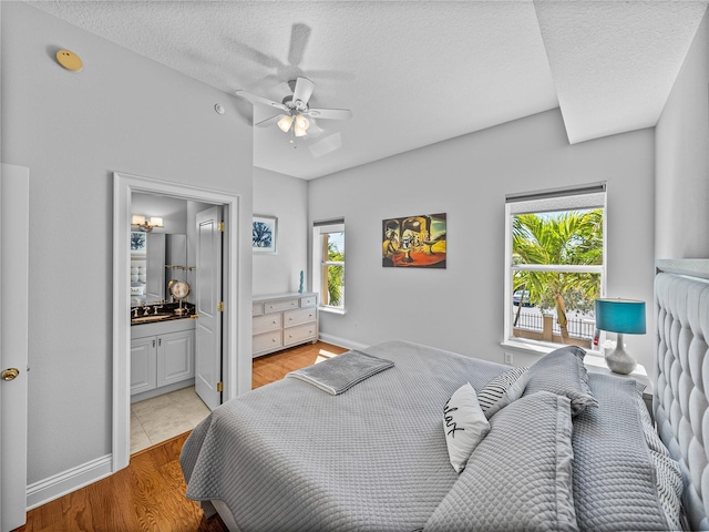 bedroom featuring a textured ceiling, connected bathroom, light wood-style flooring, and baseboards