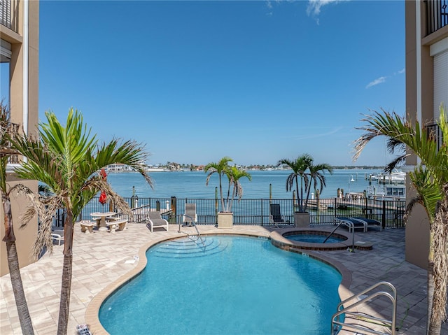 pool featuring a community hot tub, a patio area, fence, and a water view