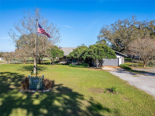 view of property hidden behind natural elements featuring gravel driveway, an attached garage, and a front yard