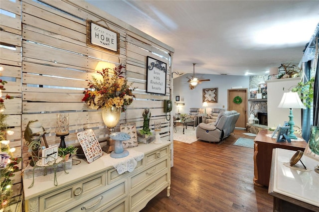 interior space with lofted ceiling, a stone fireplace, a ceiling fan, cream cabinetry, and dark wood finished floors