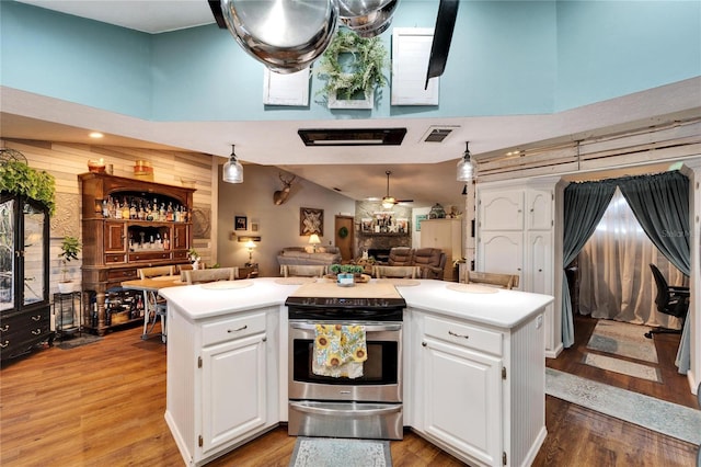 kitchen with light wood-type flooring, open floor plan, stainless steel range with electric cooktop, and a towering ceiling