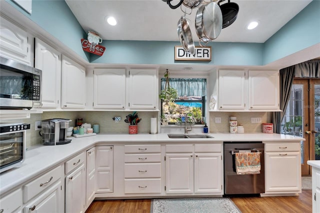 kitchen with stainless steel appliances, light wood-style floors, white cabinets, and a sink