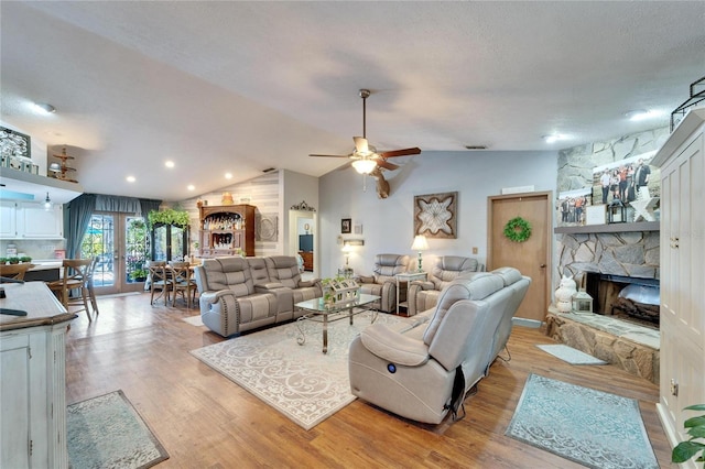 living area with lofted ceiling, a stone fireplace, and light wood-type flooring