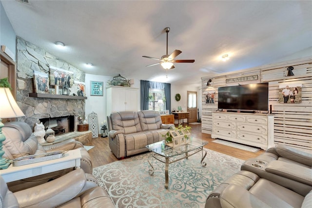 living room with light wood-type flooring, ceiling fan, vaulted ceiling, and a stone fireplace