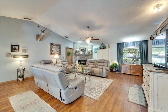 living room featuring lofted ceiling, a fireplace, visible vents, and light wood-style floors