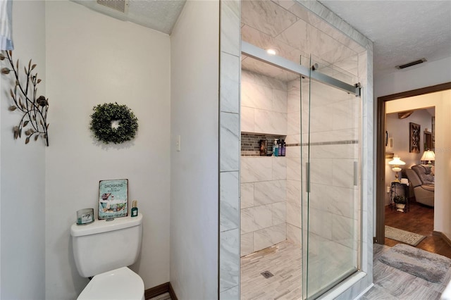 full bath featuring toilet, a shower stall, visible vents, and a textured ceiling