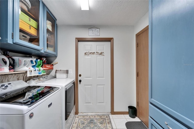 laundry area featuring light tile patterned floors, washer and clothes dryer, a textured ceiling, and cabinet space