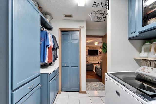 interior space featuring light tile patterned floors, washer / clothes dryer, visible vents, a textured ceiling, and blue cabinets