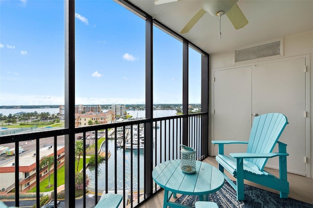 unfurnished sunroom featuring visible vents, a view of city, a ceiling fan, and a water view