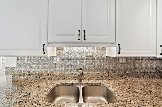 room details with a sink, light stone countertops, backsplash, and white cabinets