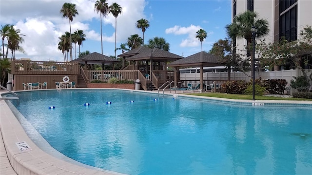 community pool with a gazebo, stairs, a deck, and fence