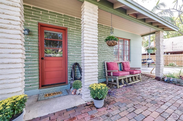 view of exterior entry with a patio area, fence, and brick siding