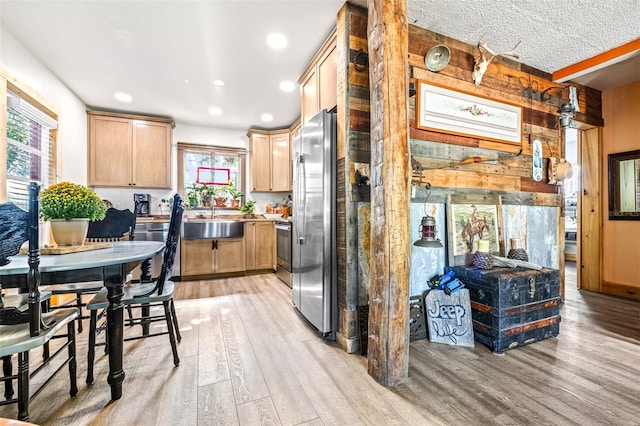 kitchen featuring light brown cabinetry, appliances with stainless steel finishes, light wood-style flooring, and wooden walls