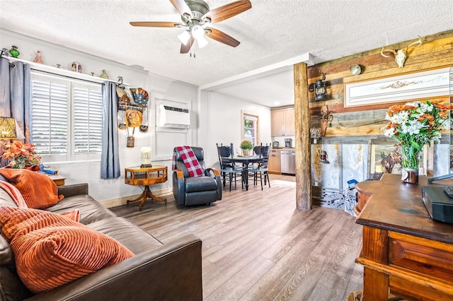 living area featuring light wood finished floors, a textured ceiling, a ceiling fan, and an AC wall unit