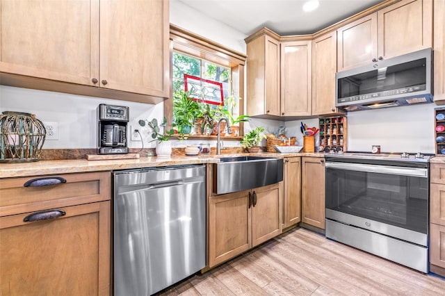 kitchen featuring stainless steel appliances, a sink, light wood-style flooring, and light stone countertops