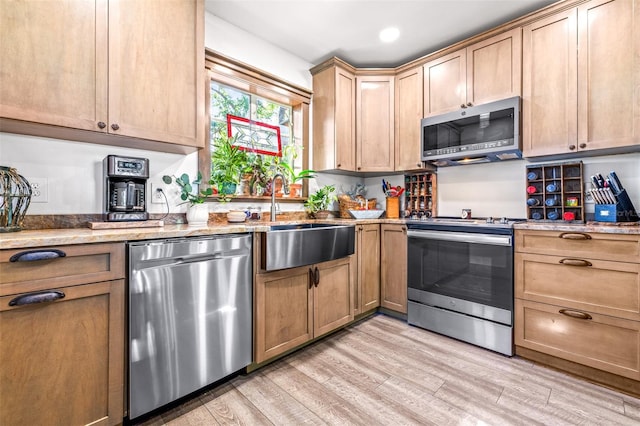 kitchen featuring light stone counters, stainless steel appliances, recessed lighting, light wood-style floors, and a sink