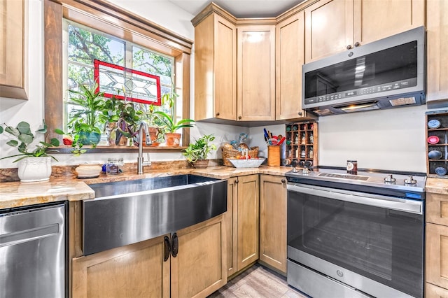 kitchen featuring stainless steel appliances, light brown cabinetry, a sink, and light stone countertops