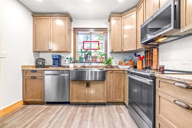 kitchen featuring stainless steel appliances, light stone counters, a sink, and light wood-style flooring